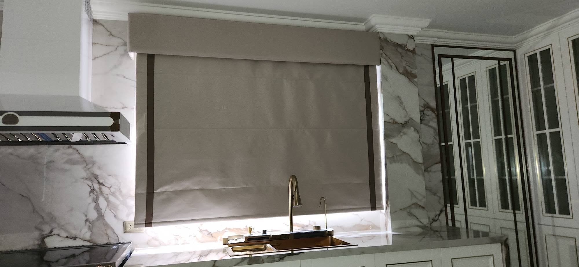 Elegant taupe Roman blind with dark trim above kitchen sink
