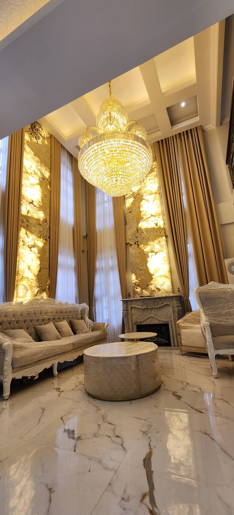 Grand double-height living room with full-length golden beige drapes and white sheer curtains
