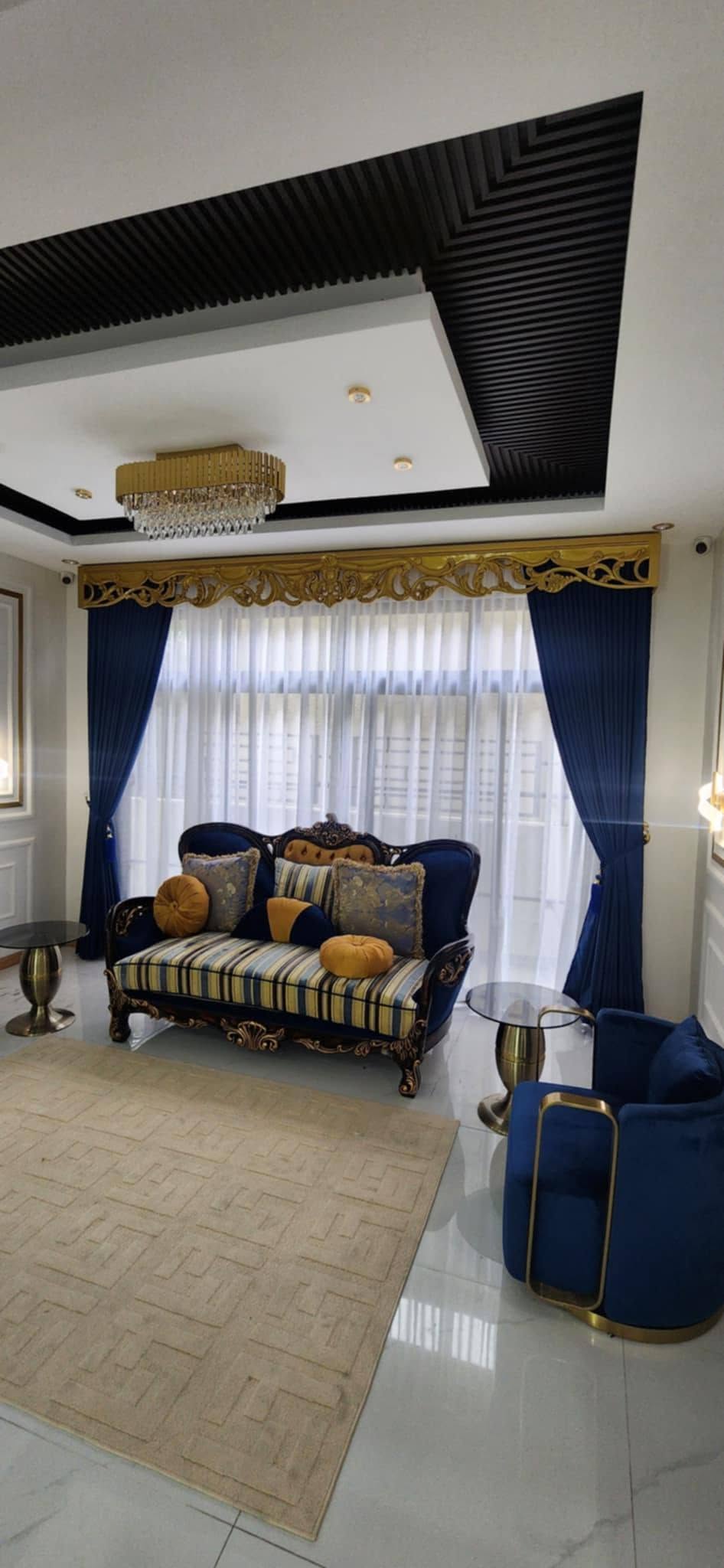 Luxury living room with royal blue velvet drapes, white S-fold sheers, and ornate gold carved valance