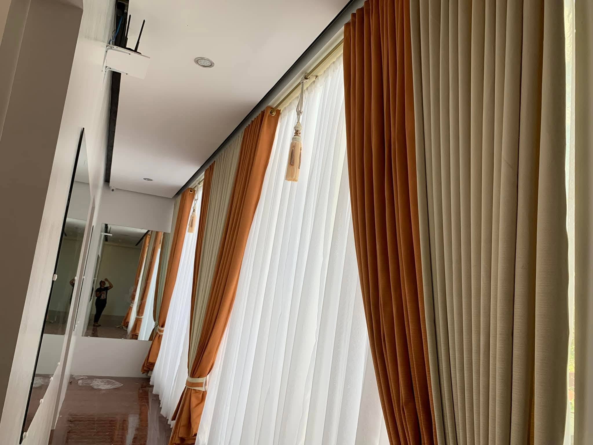 Modern layered curtains: terracotta and beige blackout drapes with white S-fold sheers along a long corridor