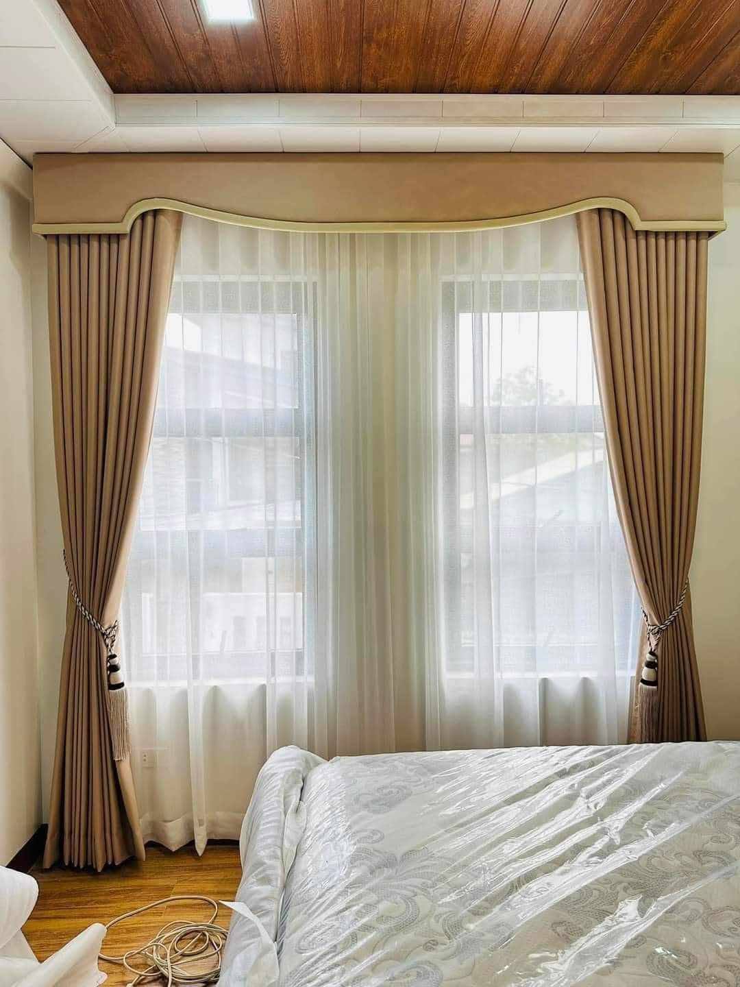 Full-height beige drapes and white S-fold sheers in a double-height living room with modern chandelier